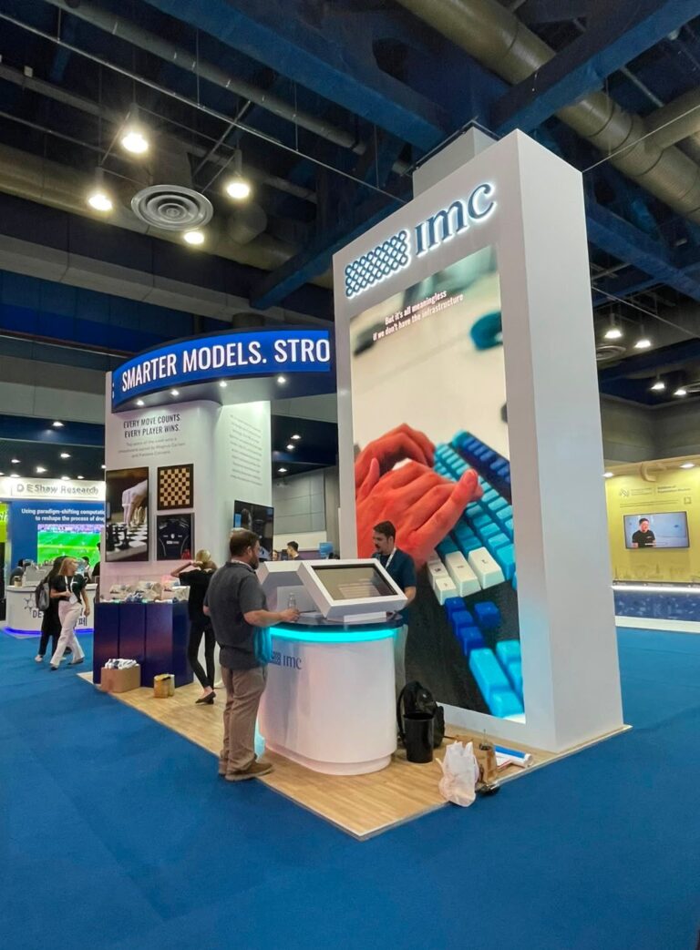 A tall white exhibition display with blue accent lighting, large product graphics and a round counter.