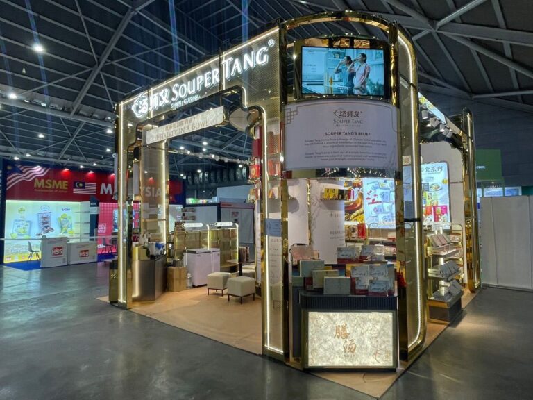 A gold framed exhibition pavilion with illuminated signs, product displays and a meeting area.