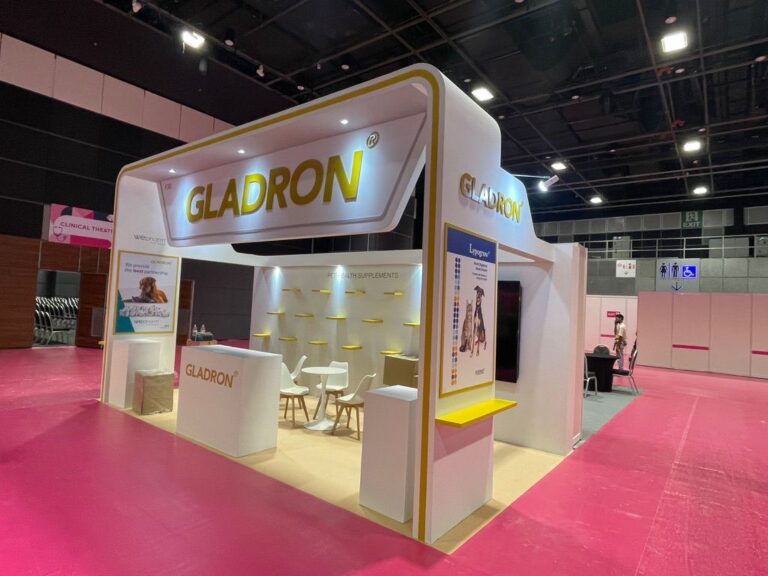 A white and gold corner exhibition stand with curved illuminated trim and open product displays.
