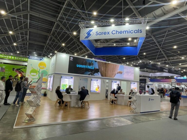 An open exhibition stand with a suspended blue and white sign, wood floor and meeting tables.